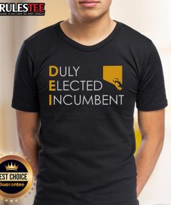 Alt Text: Top M Scott proudly wearing a Dei Duly Elected Incumbent T-shirt at a community event, promoting civic engagement.