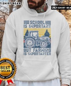 Farmer in a hoodie with 'Top School is Important but Farming is Importanter' slogan, standing next to a tractor on the farm.