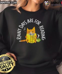 Alt Text: Cute cat in a cozy reading nook wearing a Rainy Days Are For Reading sweatshirt, perfect for cat lovers.
