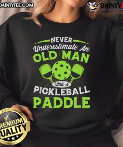 Old man confidently holding a pickleball paddle in a stylish sweatshirt that reads 'Never Underestimate An Old Man'.