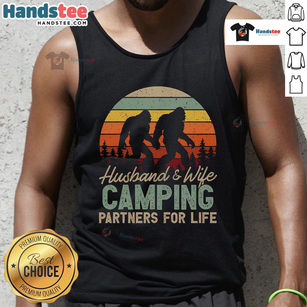 Good Bigfoot Camping Husband And Wife Partners For Life Tank Top Happy husband and wife wearing 'Good Bigfoot Camping Partners for Life' tank tops, enjoying a cozy outdoor moment.