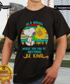 Alt Text: Happy Snoopy sunflower graphic on a retro t-shirt with the quote In a world where you can be anything, be kind.