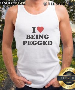 Model wearing 'Top I Love Being Pegged' tank top, showcasing bold text design in a trendy, casual setting.