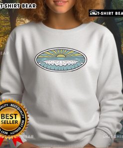 Model wearing a Nice Sunny Shore Wituka sweatshirt on the beach, showcasing a vibrant seaside style.
