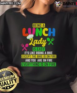 Cozy sweatshirt reading 'Being a Lunch Lady is Easy It's Like Riding a Bike Except the Bike is on Fire' for food service workers.