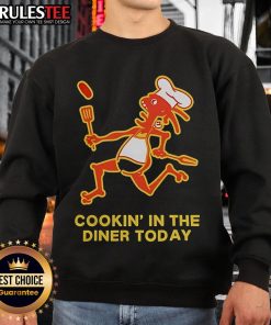 Dancing in a diner wearing a 'Good Cookin' in the Diner Today' sweatshirt, showcasing fun diner culture.