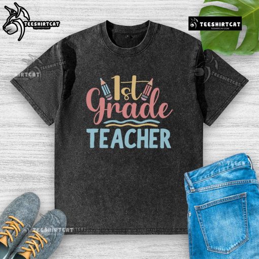 Alt Text: Pretty 1st grade teacher wearing a washed t-shirt, smiling in a colorful classroom filled with educational materials.