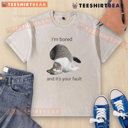 Alt Text: Funny cat looking bored in a washed t-shirt, playfully blaming its owner for the lack of fun activities.