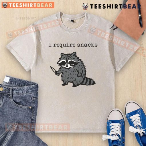 Funny 'I Require Snacks' raccoon with knife graphic on a washed t-shirt, perfect for animal lovers and snack enthusiasts.