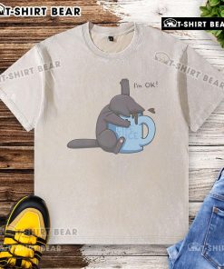 Cute cat playfully submerged in a coffee cup, wearing a I'm okay washed t-shirt, showcasing a humorous moment.
