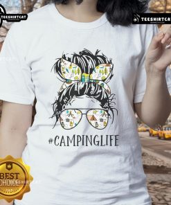 Mom in a messy bun enjoying camping life, wearing a 'Pretty Camping Life' tee, surrounded by nature.