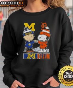 Alt Text: Cozy sweatshirt featuring Snoopy and Charlie Brown, showcasing Michigan Wolverines and Detroit Tigers skyline design.