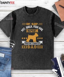 Alt Text: Adorable Miniature Schnauzer on a dad wearing a washed T-shirt with 'Eat, Sleep, Walk, Feed Dog' slogan.