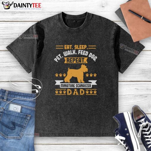 Alt Text: Adorable Miniature Schnauzer on a dad wearing a washed T-shirt with 'Eat, Sleep, Walk, Feed Dog' slogan.