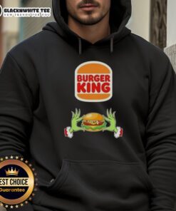 Happy Grinch hands holding a burger, wearing a Merry Christmas hoodie at Burger King, celebrating the festive season.