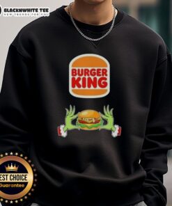 Happy Grinch hands holding a burger, wearing a Merry Christmas sweatshirt from Burger King, perfect holiday cheer.