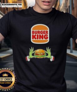 Alt Text: Happy Grinch hands holding a burger, wearing a 'Merry Christmas' T-shirt from Burger King, festive holiday spirit.