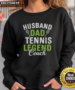 Happy husband and dad wearing a Tennis Legend Coach sweatshirt, smiling on the court with a tennis racket in hand.