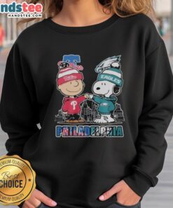 Alt Text: Official Philadelphia Phillies and Eagles 75th Anniversary Peanuts Snoopy sweatshirt featuring vibrant team logos.