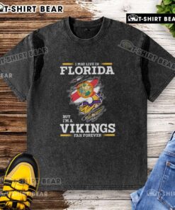 Gray washed t-shirt with 'I May Live In Florida But I'm A Minnesota Vikings Fan Forever' text, showcasing team pride.