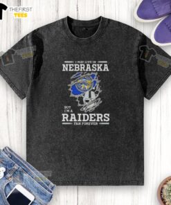 Top I May Live in Nebraska But I'm a Raiders Fan Forever washed t-shirt displayed on a hanger in casual setting.
