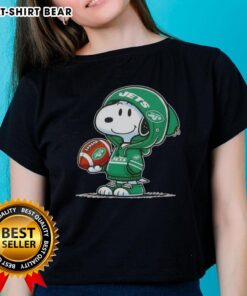 Official Peanuts Snoopy in a hoodie smiling at fans, promoting New York Jets ladies tee merchandise.