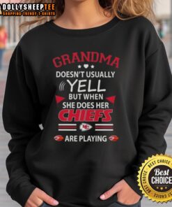 Awesome grandma in a Kansas City Chiefs sweatshirt, cheering passionately during a football game.