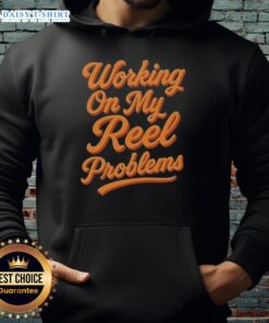 Person wearing an Awesome Working On My Reel Problems Fishing Hoodie while fishing by the lake, enjoying outdoor life.
