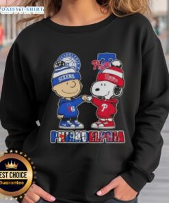 Alt Text: Cute Charlie Brown fist bump with Snoopy on 76ers x Phillies sweatshirt, perfect for Philadelphia sports fans.