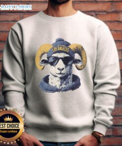 Los Angeles Rams mascot in a beanie and sunglasses, wearing a sweatshirt, cheering at a football game.