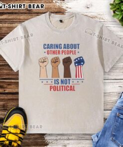 Nice caring about other people is not political fists washed t-shirt displayed on a hanger in a bright room.