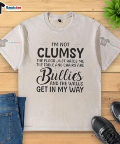 Alt Text: Premium I'm Not Clumsy, The Floor Just Hates Me washed t-shirt displayed on a wooden table with chairs.