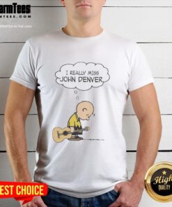 Alt Text: Charlie Brown holding a guitar, wearing a I Really Miss John Denver t-shirt, showcasing a nostalgic tribute.