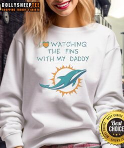 Adorable child in a Miami Dolphins sweatshirt, happily watching dolphins with dad at the beach, showcasing family fun.