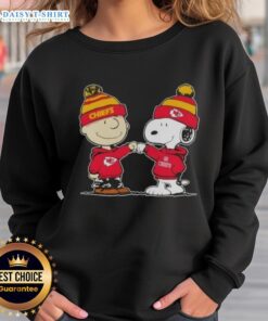 Charlie Brown and Snoopy fist bump in Kansas City Chiefs football sweatshirt, celebrating friendship and team spirit.