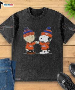 Charlie Brown and Snoopy fist bump on a Denver Broncos football washed t-shirt, perfect for Peanuts fans and sports lovers.
