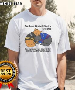 Two male cats playfully fighting and then napping together in a closet, featured on a 'Heated Rivalry' T-shirt.