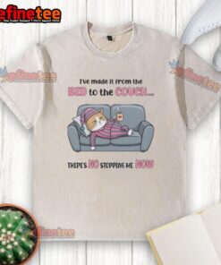 Alt Text: Tired cat wearing a washed t-shirt lounging on the couch after making the leap from the bed, looking relaxed.