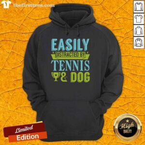 Dog wearing a 'Funny Easily Distracted by Tennis' hoodie, playfully looking at a tennis ball in a sunny park.