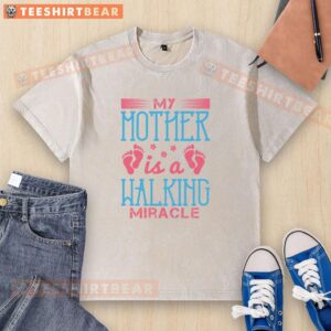 Alt Text: Good My Mother Is A Walking Miracle washed t-shirt displayed on a hanger, featuring a bold inspirational graphic design.