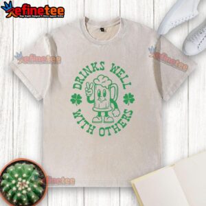 Official St. Patrick's Day washed t-shirt featuring 'Drinks Well With Others' design and shamrock graphic.