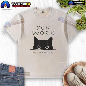 Black cat lounging on a t-shirt reading 'You work, I watch and judge' - perfect for cat lovers and humor enthusiasts.