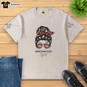 Alt Text: Official Denver Broncos girl wearing messy bun and glasses, showcasing a stylish washed t-shirt in team colors.