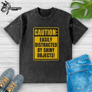 Top caution easily distracted by shiny objects washed t-shirt design featuring playful graphics and vibrant colors.