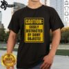 Top Caution Easily Distracted By Shiny Objects T-Shirt design featuring bold text and playful graphics in vibrant colors.