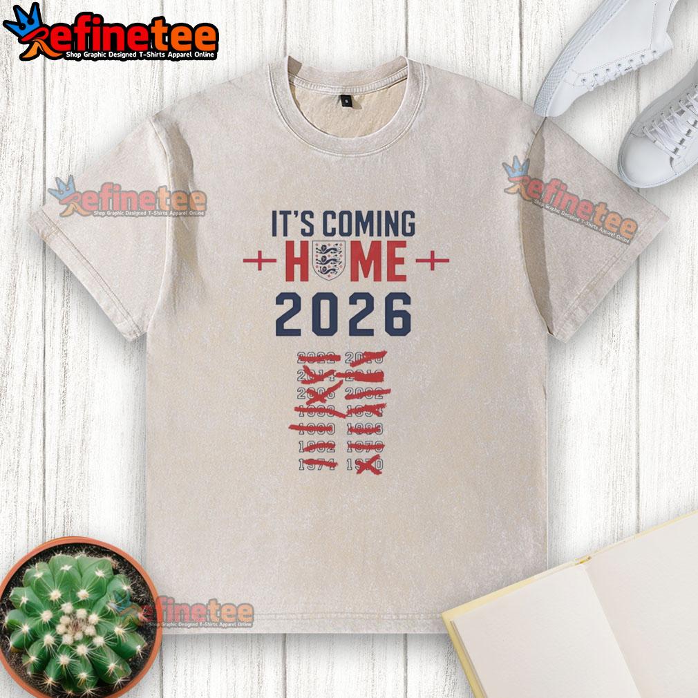 awesome-its-coming-home-2026-england-national-football-washed-t-shirt Awesome It's Coming Home 2026 England National Football washed t-shirt displayed on a wooden table with soccer elements.