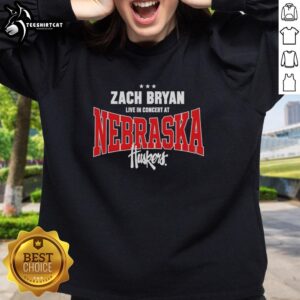 Zach Bryan live in concert wearing a Nebraska Huskers sweatshirt, captivating the audience with his performance.